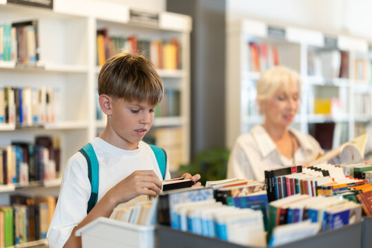 Interested teen male visitor holding a book near display stand in public library