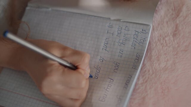 Angled close view of hand actively writing numbers and checkmarks on gridded notebook page with pen, showing organized notes, tallies, and calculations in focused study workspace, with hand, writing