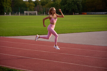 Fototapeta premium Fit female athlete running on an outdoor stadium track featuring a green grass field background