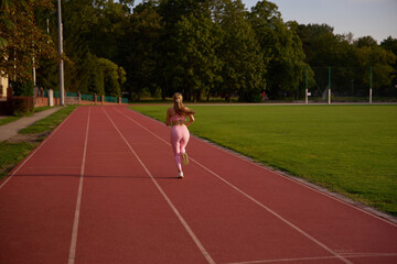 Fototapeta premium Active outdoor fitness, physical exercise, and athletic wellness concept. Young woman sprinting on a sports track. Female runner in motion during beautiful golden hour sunlight