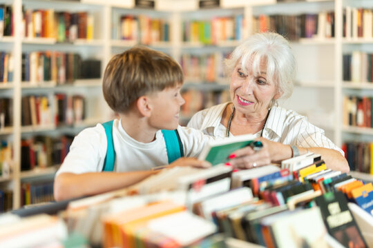 Teen boy with grandmother customer flips through book in sales area of store or library, picks up reading material, hobbies or way to pass evening.