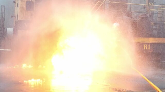 Firefighter industrial fire hose water spray refinery emergency response training drill, protective suit, high pressure stream tackling fuel blaze, flame smoke explosion danger night fireball debris