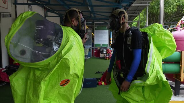 Hazmat suit chemical protection respirator safety emergency training decontamination drill in industrial facility, rescue team in green gas tight coveralls and masks for spill response exercise
