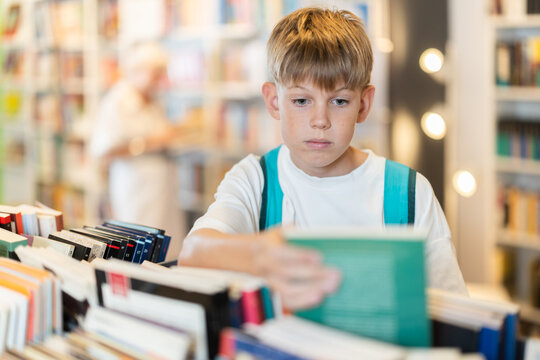 Interested teen male visitor holding a book near display stand in public library