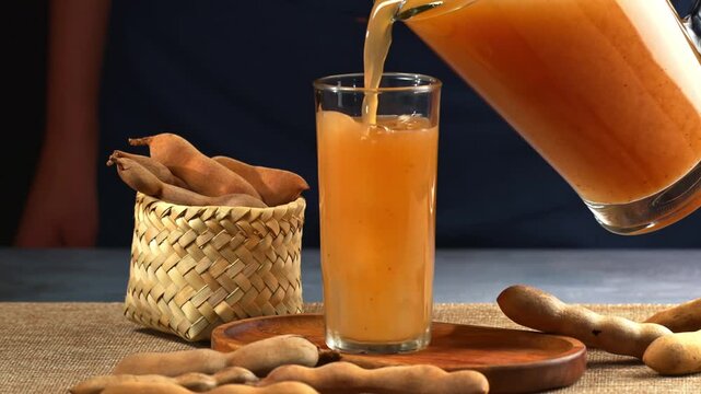 Woman pouring fresh tamarind juice into a glass with ice cubes