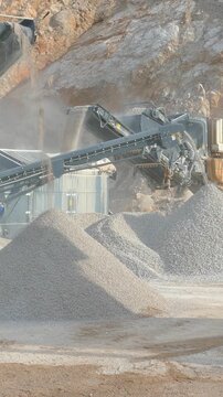 Stone crushing machine at open pit mining and processing plant for crushed stone. Piles of gravel stone and conveyor belts. Excavator loading rocks. Concepts of industry and building materials