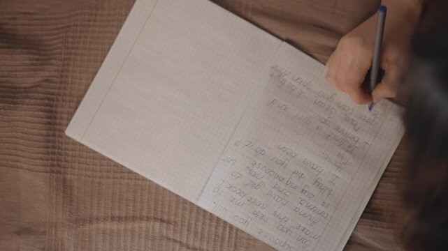 Top down scene showing right hand holding pen and making repetitive marks across large sheet of paper laid on brown textured fabric, with calm focus, creative planning, and tactile home workspace mood