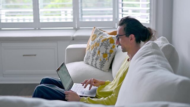 Man Typing on Laptop Beside Floral Cushion on Couch 4K