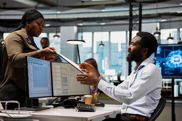 Fototapeta premium Smiling coworker gives paperwork to a software developer focused on coding at an office workstation.