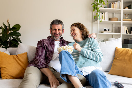 Happy couple laughing watching movie eating popcorn at home