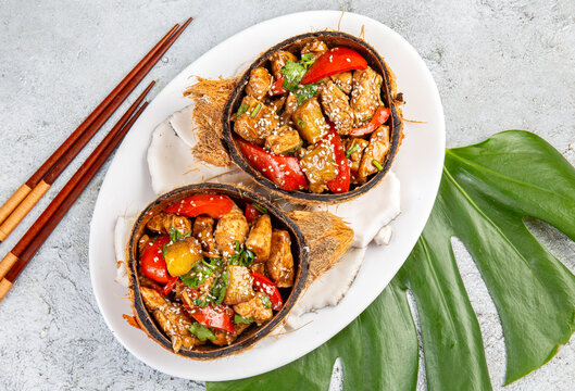 Hawaiian pinapple chicken in natural coconut shell plates on white background