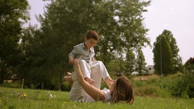 Playful mother lifting her son with legs in a sunny park