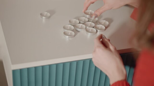 High angle close view shows hands sorting white round pills on pale countertop beside teal fluted cabinet, with careful counting, stacking, and placing actions over scattered tablets nearby