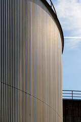 Curved corrugated metal silo wall with vertical lines and sunlight © Dina