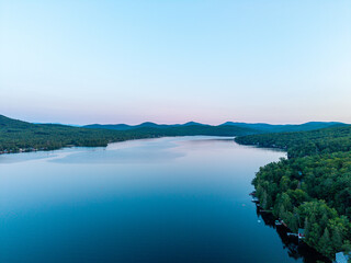 Fototapeta premium Maidstone Lake, Vermont, high aerial drone view at dusk, showing calm waters reflecting the soft twilight sky over surrounding mountains and forested shorelines.