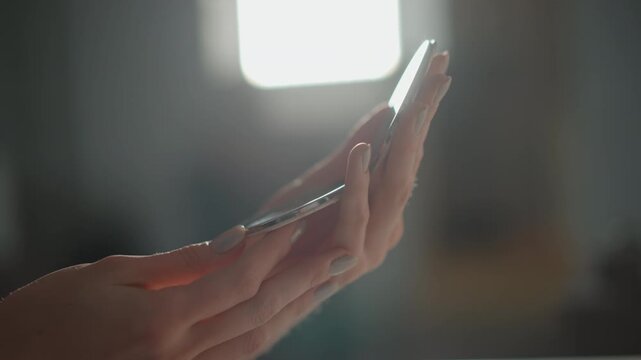 Hands gently hold thin reflective object near window light while fingers make careful adjustments, revealing soft highlight, subtle upward movement and quiet focused inspection, with hand, holding