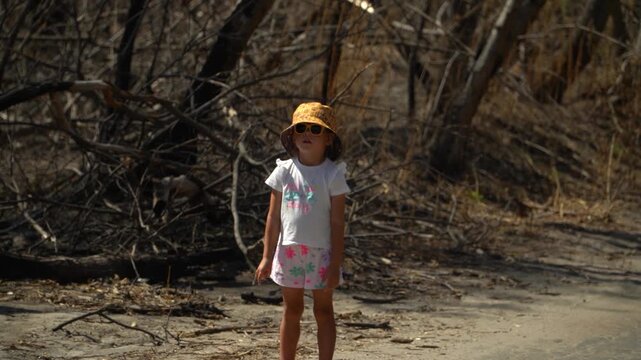 A little girl looks with interest aftermath of a forest fire, trees without leaves and branches, dead wood, asks and inquires about the reasons, turns her head, a sunny spring day.