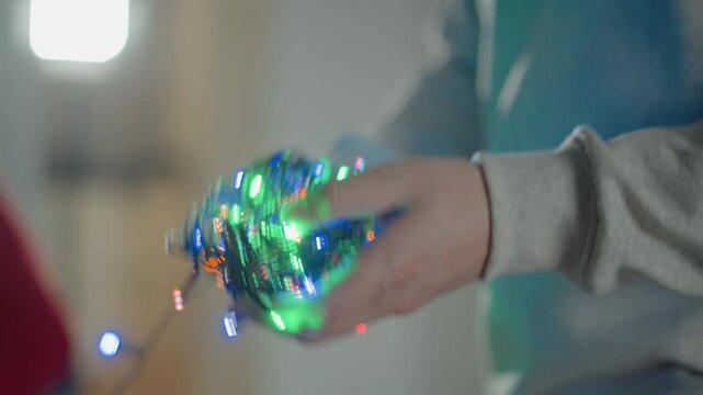 Close view of hands actively separating, testing, and arranging glowing multicolored holiday lights indoors, with loose cable, warm illumination, soft bokeh, and cozy festive mood, with hand, light