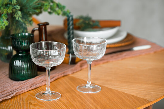 Elegant festive table setting with empty glasses, evergreen branches, candles and dinnerware on a wooden table, creating a warm atmosphere for Christmas or holiday celebrations.