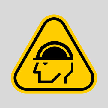 Yellow triangular warning sign featuring a person wearing a hard hat, indicating a head protection hazard.