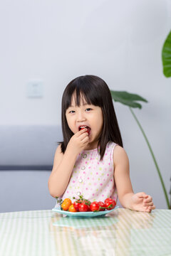 Asian little girl eating fresh cherry tomatoes, healthy diet and nutrition concept