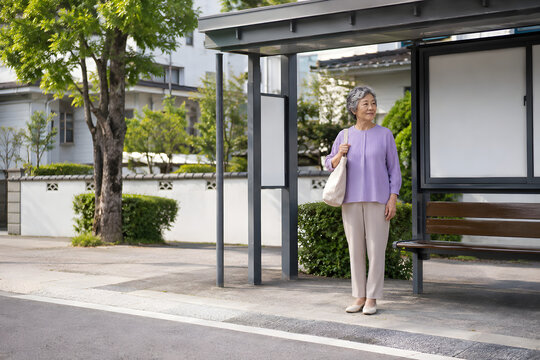 Older Asian woman waiting at community shuttle pickup point with tote bag