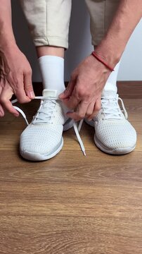 Close up of a woman tying shoelaces on white sneakers indoors. Sport shoes on wooden floor. Preparing for workout, fitness, jogging, training or daily casual activity.