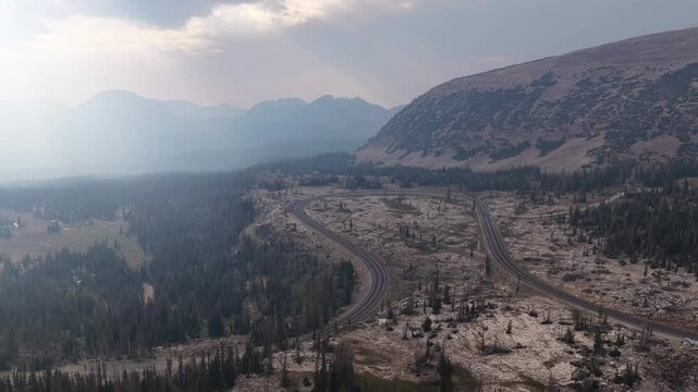 Aerial of Bald Mountain Pass highway in Uinta Wasatch Cache National Forest with layers of mountains receding into the distance under a hazy sky in Utah in summer