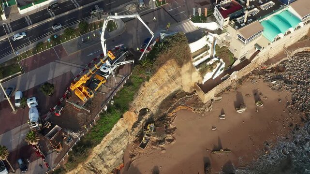 Workers take action to stop soil erosion on the beach in Sao Pedro do Estoril aerial view. Heavy machinery is used to restore the land and protect property from further damage.