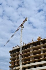 A shot of a tall construction tower crane operating next to a modern multi-story residential building under construction against a blue cloudy sky. Ideal for real estate development, architecture © Drachenfutter