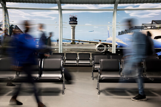 Fast-moving passengers create blurred motion inside a busy airport lounge, navigating a crowded transit hub on a long layover ahead of their next international departure while carrying luggage.