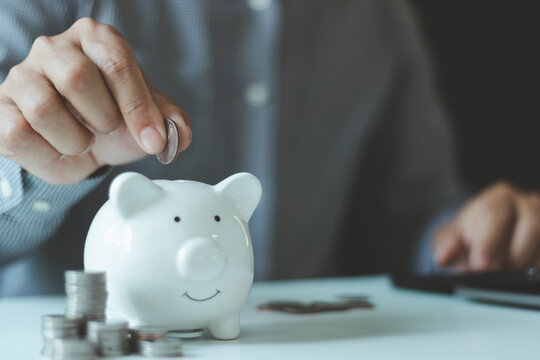 Saving money concept with a piggy bank, coins, and a person putting money aside for personal finance, budgeting, financial planning, savings goals, and responsible wealth management at home.