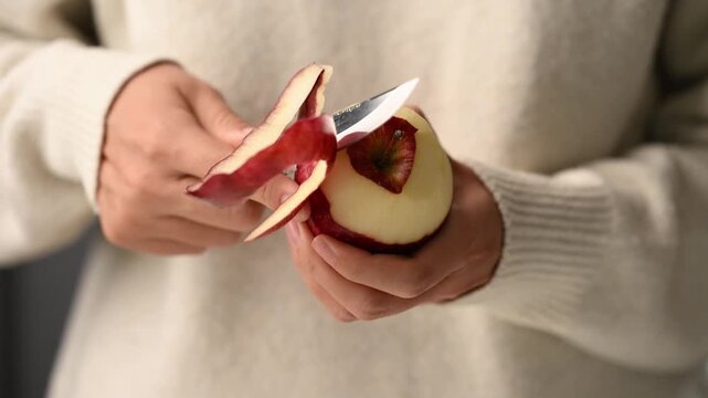 Close up of woman hands peeling a fresh red delicious apple with a paring knife, Healthy eating