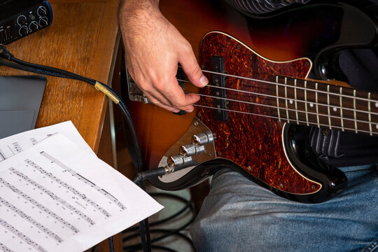Musician playing electric bass guitar while reading sheet music during a music practice session. Concept of musical education, rehearsal, performance, technique and learning an instrument