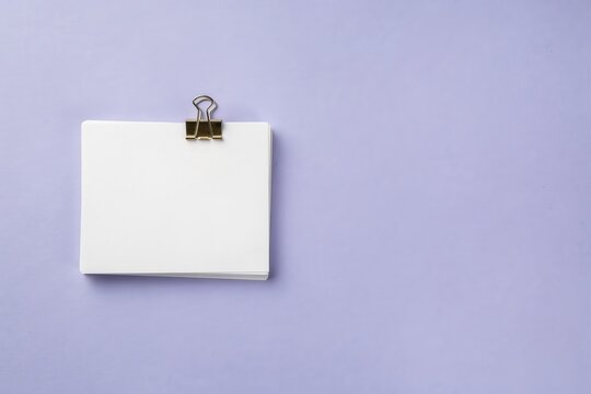 Minimalist white paper stack with metal binder clip. Blank note card on purple background. Clean office stationery mockup.