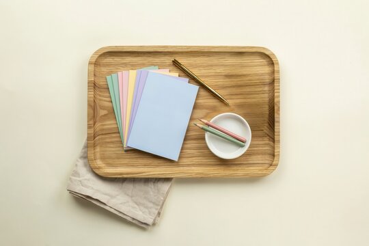 Minimalist pastel stationery set on wooden tray, colorful paper cards with pencils and brass tool, aesthetic desk flat lay