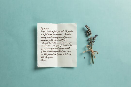 Vintage folded paper letter with handwritten cursive text and dried lavender sprig on pastel blue background. Romantic concept for love note, miss you message