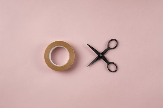 Minimalist adhesive tape and scissors on pink background. Flat lay stationery objects for crafting and design. Clean workspace with packing materials for copy space.