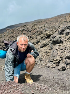 Tourist on the surface of the active volcano Etna. A man touches the hot stones on the volcano during a tour. Free space for text.