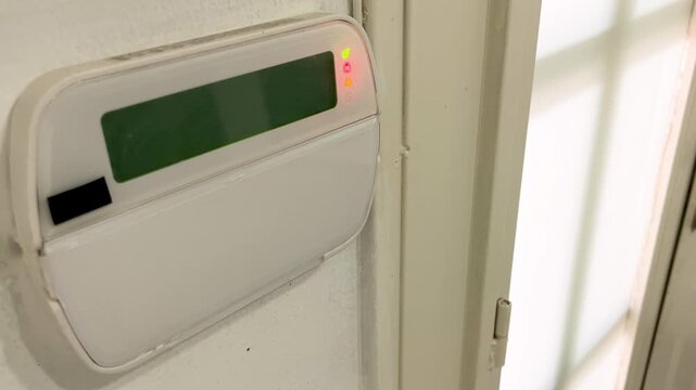 Home security alarm panel keypad with a red light blinking, indicating the system is armed for surveillance, burglary prevention, and monitoring of the armored door