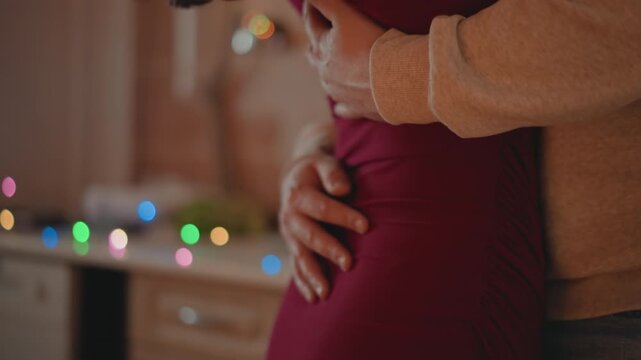 Expectant couple share intimate embrace in cozy kitchen, leaning forehead to forehead while partner cradles head and back and expectant woman wraps arms around neck in calm loving home setting