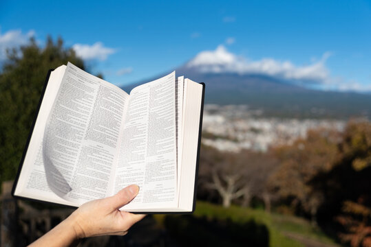 Outdoors, an open Bible showing Psalms is held by a hand against Mount Fuji and Fujinomiya city from Shirao Mountain Park (Shiraosan).