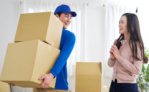 段ボールを持つ引っ越し業者と笑顔で指示する女性