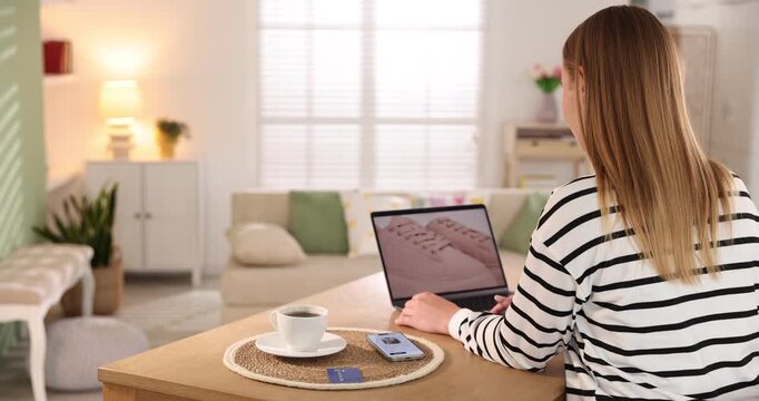 Online store. Woman with credit card using laptop at wooden table indoors, back view
