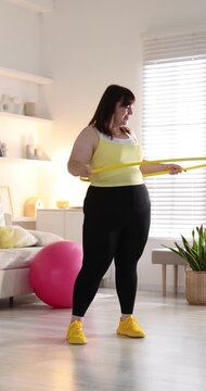 Overweight woman exercising with hula hoop indoors. Sports equipment