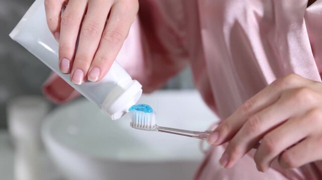 Woman applying toothpaste on toothbrush in bathroom, closeup
