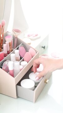 Woman putting cream into makeup organizer at table indoors, closeup