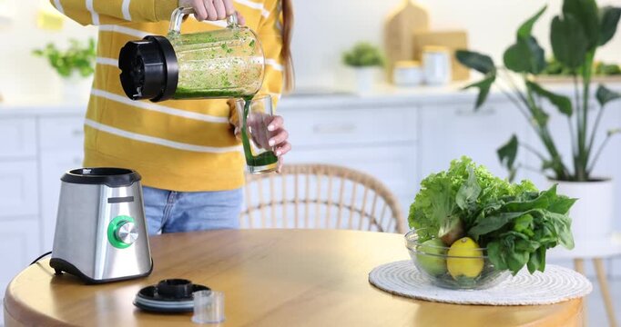 Woman pouring green smoothie into glass from blender at wooden table indoors, closeup