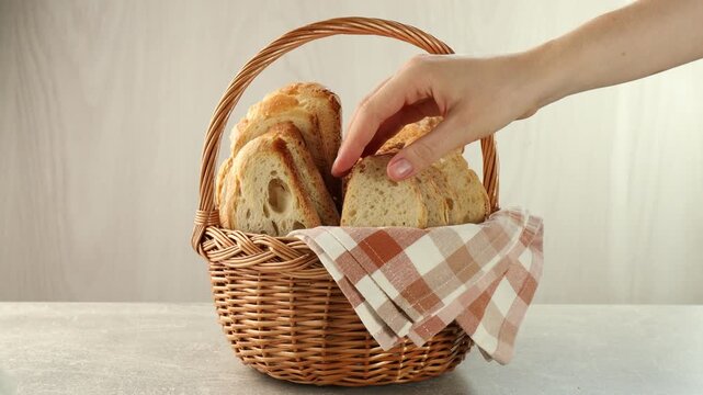 Woman putting wicker basket with bread and taking slice on table, closeup