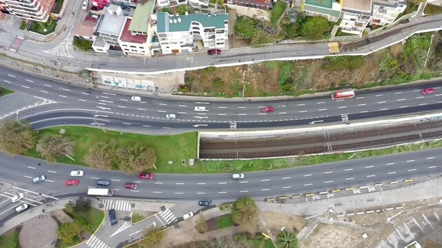 Top down drone view of moving traffic along urban roads beside railway tracks, residential buildings and green areas, showing transportation infrastructure and city mobility.